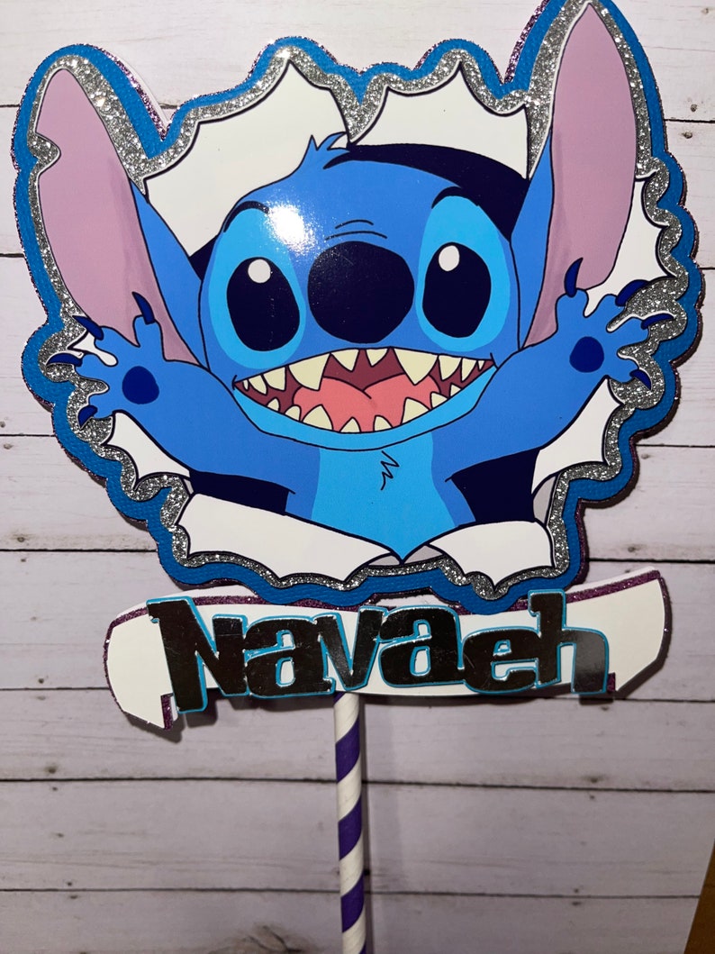 Może przedstawiać: Topper na tort z niebieskim Stitch'em, srebrną błyszczącą ramką i imieniem "Navaeh" napisanym srebrnymi błyszczącymi literami.