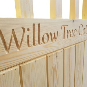 May include: A wooden sign with the words "Willow Tree Cottage" carved into it. The sign is made of light-coloured wood and has a rustic look.