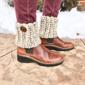 May include: A pair of brown leather ankle boots with beige crocheted boot cuffs. The boot cuffs have a button detail.