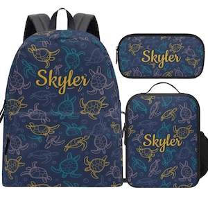 Könnte beinhalten: Ein marineblaues Set aus Rucksack, Federmäppchen und Lunch-Tasche. Das Set zeigt ein Muster aus bunten Meeresschildkröten und den Namen "Skyler" in goldener Schrift. Der Rucksack hat graue Träger.
