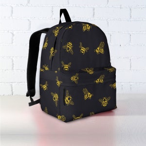 May include: Black backpack with a repeating pattern of yellow bees. The backpack has a front pocket, black straps, and a top handle. The bee design is a simple illustration.