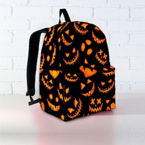 May include: Black backpack with a repeating pattern of orange jack-o'-lantern faces. The backpack has black straps, a top handle, and a front pocket. The design is perfect for Halloween.