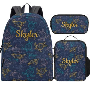 May include: A navy blue backpack, pencil case, and lunch bag set. The set features a pattern of colourful sea turtles and the name "Skyler" in gold script. The backpack has black straps and a grey back.