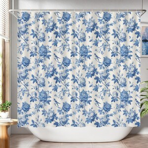 May include: A floral shower curtain featuring a repeating pattern of blue roses, leaves, and small birds on a cream background. The curtain is hanging in front of a white bathtub. The design has a vintage, botanical theme.