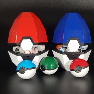 Może przedstawiać: Dwa pojemniki w kształcie Pokeballa, jeden czerwony, a drugi niebieski, z białą podstawą i czarnymi akcentami. Każdy pojemnik jest wypełniony małymi, kolorowymi kulkami. Trzy Pokeballe, jeden niebieski, jeden zielony i jeden czerwony, znajdują się przed pojemnikami.