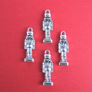 May include: Four silver-toned nutcracker charms, each featuring a detailed design of a soldier in a traditional uniform. The charms are perfect for adding a festive touch to jewellery or crafts.