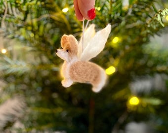 May include: A felt Christmas ornament of a dog with white wings. The dog is brown and white and is flying in the air.