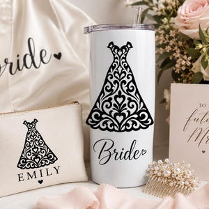 May include: A white tumbler with a black dress design and the word "Bride". A matching cosmetic bag with the name "Emily" and a dress design. A white robe with the word "Bride". A card that says "To my future Mrs."