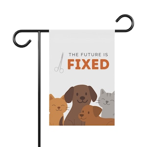 May include: A white garden flag with the text "THE FUTURE IS FIXED" in orange and black. The flag features illustrations of a brown dog, two orange cats, a brown dog, and a gray cat. A pair of scissors is also shown.