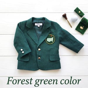 May include: A forest green blazer featuring a notched lapel, two gold-tone front buttons, and two gold-tone buttons on each cuff. A circular patch depicting a map of the United States is on the left chest. Includes a golf tee, ball, and pin.