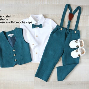 May include: A formal teal outfit for a young child, including a vest, a white cotton shirt, teal pants with suspenders, a teal bow tie, and white shoes. The set is displayed on a light wood surface.