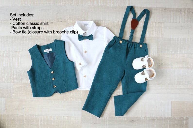 May include: A formal teal outfit for a young child, including a vest, a white cotton shirt, teal pants with suspenders, a teal bow tie, and white shoes. The set is displayed on a light wood surface.