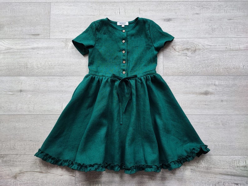May include: A green linen dress with short sleeves, a button-up front, and a ruffled hem.