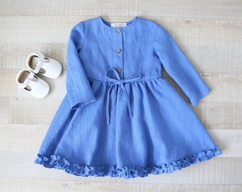 May include: A blue linen dress with long sleeves, a button-up front, and a tie at the waist. The dress has a ruffled hem.