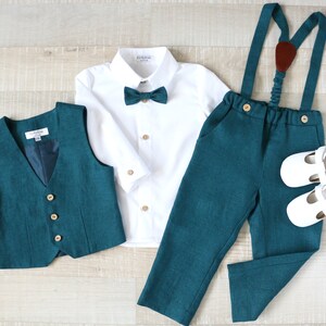 May include: A teal green formal outfit for a child, including a vest, pants with suspenders, a white button-down shirt, a bow tie, and white shoes. The vest and pants have wooden buttons.