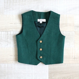 May include: A dark green vest with a V-neck and three wooden buttons. The vest has a dark green lining and a small tag with text. The vest is made of a textured fabric.