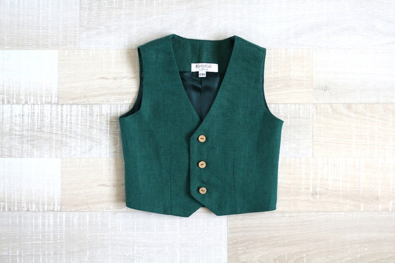 May include: A dark green vest with a V-neck and three wooden buttons. The vest has a dark green lining and a small tag with text. The vest is made of a textured fabric.