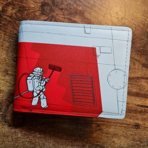 Op de afbeelding: Een bi-fold portemonnee met een rood en wit ontwerp. De voorkant heeft een cartoon illustratie van een persoon in een gevaarlijk pak met een raamtrekker. De portemonnee heeft een witte binnenkant en een gestikte rand.