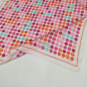 May include: White silk scarf with a polka dot pattern in pink, orange, and blue. The dots are large and the scarf has a thin yellow border. The word "CELINE" is printed in yellow at the bottom of the scarf.
