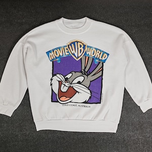 Peut inclure: Sweat-shirt blanc à manches longues avec un motif de Bugs Bunny. Le motif représente Bugs Bunny avec les mots "Movie World" et "Gold Coast, Australie".