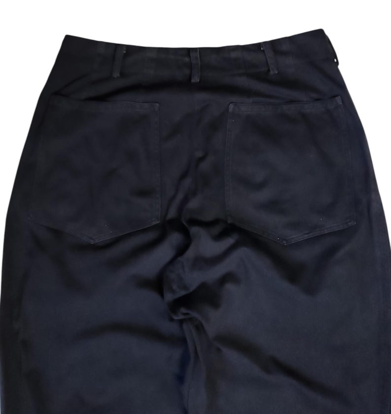 Puede incluir: Primer plano de la parte trasera de unos pantalones negros. Los pantalones tienen dos bolsillos cuadrados grandes y una cintura con trabillas. La tela parece ser un material oscuro y resistente.