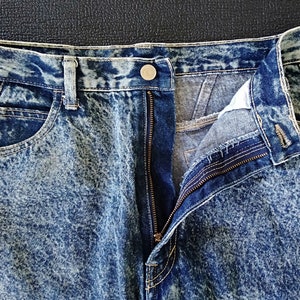 Może przedstawiać: Dżinsy z efektem acid wash z zamkiem błyskawicznym i guzikiem. Dżinsy są jasnoniebieskie z białym wzorem w kropki.