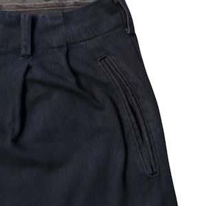 Puede incluir: Primer plano de un pantal&oacute;n azul marino con la parte delantera plisada y un detalle de bolsillo. El pantal&oacute;n tiene un dise&ntilde;o cl&aacute;sico con cierre de bot&oacute;n y cremallera. La tela parece ser un material resistente, adecuado para el uso diario.