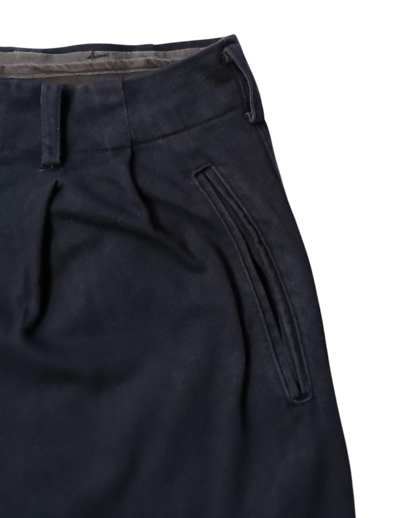 Puede incluir: Primer plano de un pantal&oacute;n azul marino con la parte delantera plisada y un detalle de bolsillo. El pantal&oacute;n tiene un dise&ntilde;o cl&aacute;sico con cierre de bot&oacute;n y cremallera. La tela parece ser un material resistente, adecuado para el uso diario.