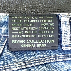 Może przedstawiać: Czarna sk&oacute;rzana naszywka z białym tekstem na niebieskich dżinsach. Tekst brzmi: "FOR OUTDOOR LIFE AND TOWN CASUAL IT'S GREAT COMFORT AND BETTER FIT. NOW, WE MEET WITH FRESH SENSATION -WE JOIN THE PEOPLE OF HIGHLY SENSITIVE TO FASHION. RIVER COLLECTION ORIGINAL JEANS"