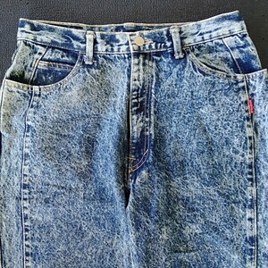 Może przedstawiać: Dżinsy niebieskie z efektem acid wash, z guzikowym zapięciem i czerwoną metką "Sport Club" na prawej tylnej kieszeni.