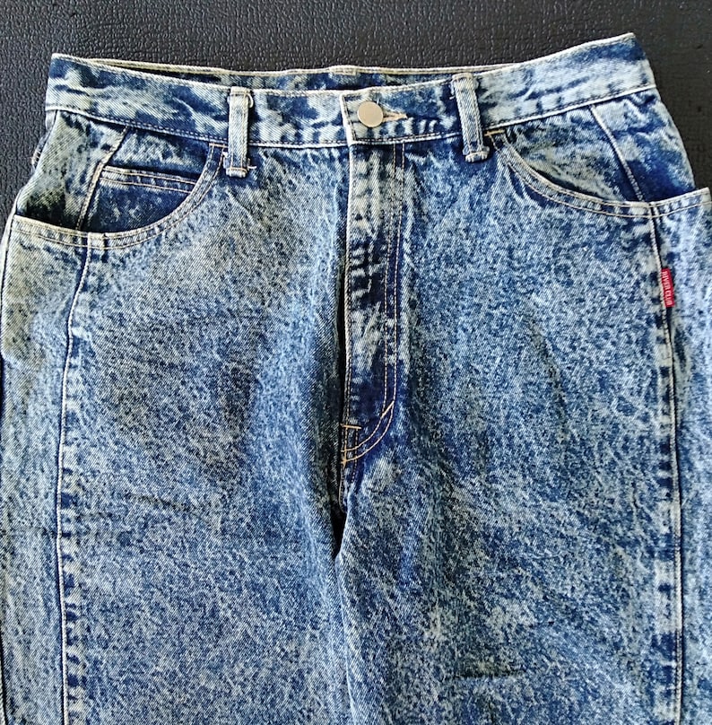 Może przedstawiać: Dżinsy niebieskie z efektem acid wash, z guzikowym zapięciem i czerwoną metką "Sport Club" na prawej tylnej kieszeni.