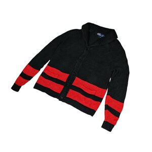 May include: Black cardigan sweater with red stripes and a shawl collar. The sweater has a button closure and two pockets.