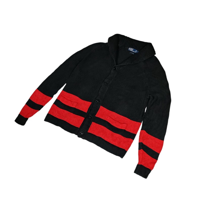 May include: Black cardigan sweater with red stripes and a shawl collar. The sweater has a button closure and two pockets.