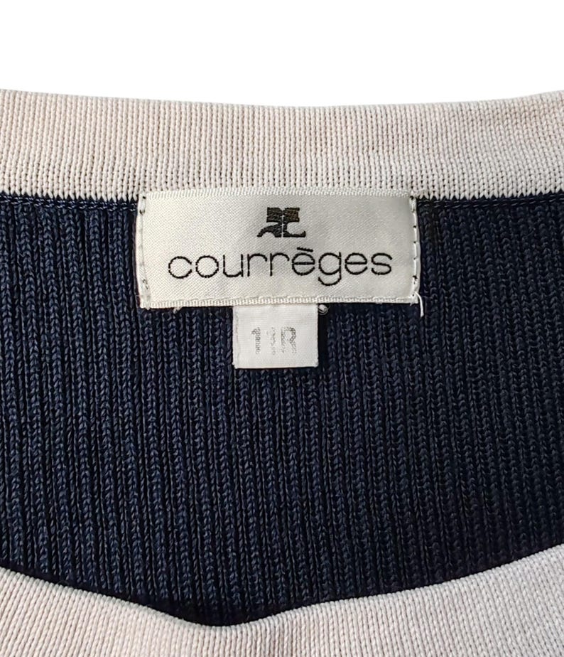 May include: A navy blue and cream ribbed knit garment featuring a white rectangular brand label stitched at the neckline. The label displays the text courr&egrave;ges with a logo above it and a smaller tag below with the text 11R printed in black.