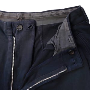 Puede incluir: Primer plano de pantalones azul marino con cremallera y cierre de bot&oacute;n visibles. Los pantalones tienen un dise&ntilde;o cl&aacute;sico, con una vista detallada de la cintura y los bolsillos. La tela parece ser un material resistente.