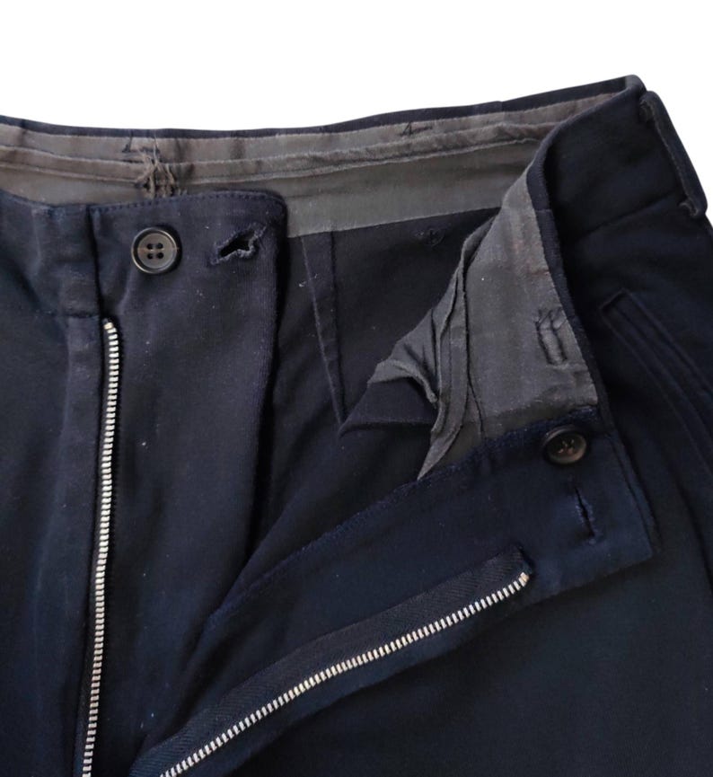 Puede incluir: Primer plano de pantalones azul marino con cremallera y cierre de bot&oacute;n visibles. Los pantalones tienen un dise&ntilde;o cl&aacute;sico, con una vista detallada de la cintura y los bolsillos. La tela parece ser un material resistente.