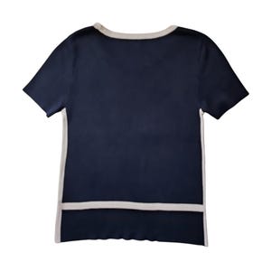 May include: A short-sleeved navy blue knit top featuring a contrasting light beige trim along the round neckline, the side seams, and a horizontal band across the lower section of the garment, creating a clean and structured visual appearance.