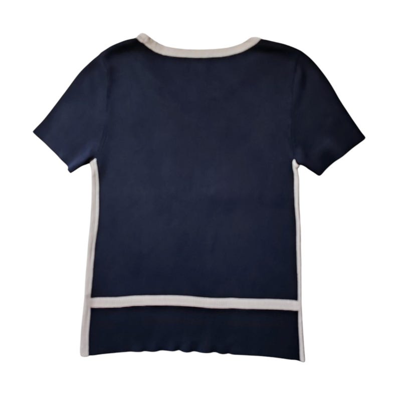 May include: A short-sleeved navy blue knit top featuring a contrasting light beige trim along the round neckline, the side seams, and a horizontal band across the lower section of the garment, creating a clean and structured visual appearance.