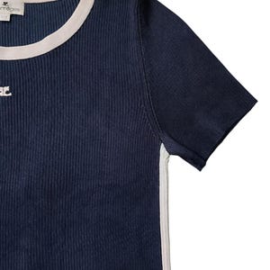 May include: A dark navy blue ribbed knit t-shirt featuring a cream-colored crew neckline and matching side panels. The garment includes a small embroidered logo on the chest and a brand label at the neck that reads Courr&egrave;ges.