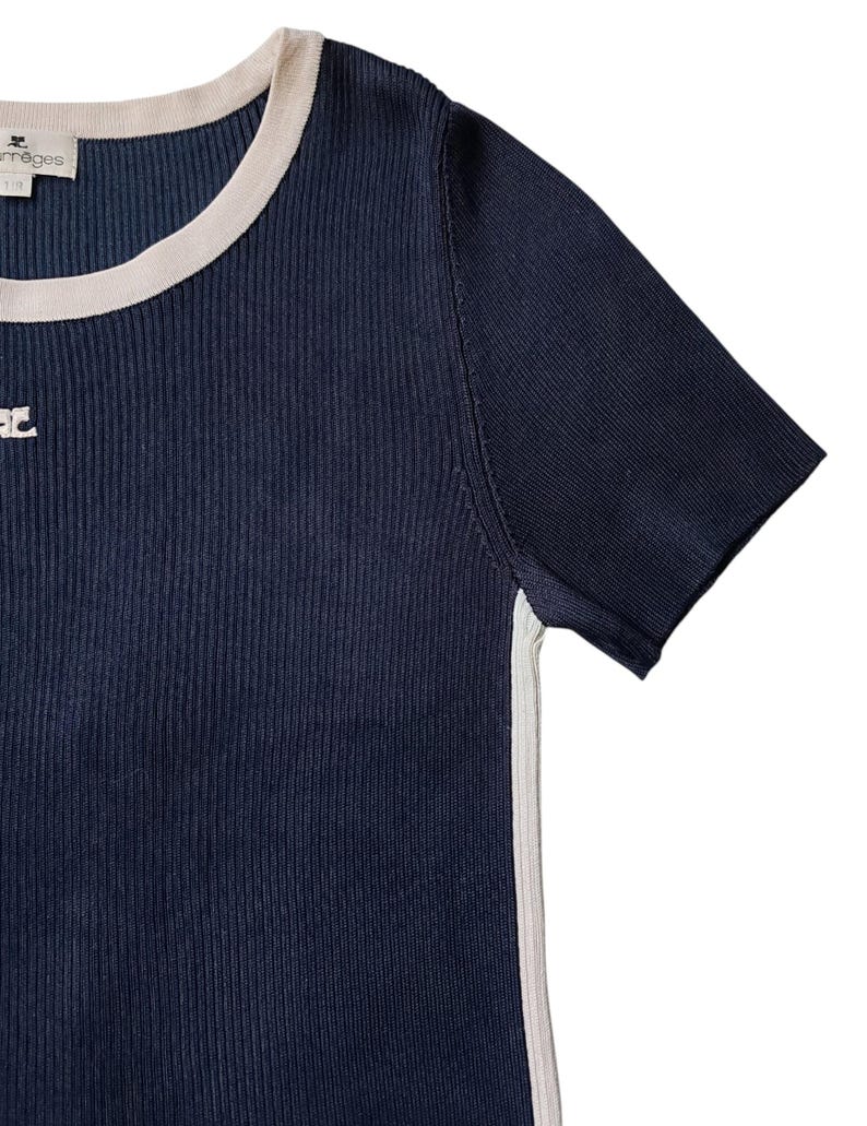 May include: A dark navy blue ribbed knit t-shirt featuring a cream-colored crew neckline and matching side panels. The garment includes a small embroidered logo on the chest and a brand label at the neck that reads Courr&egrave;ges.