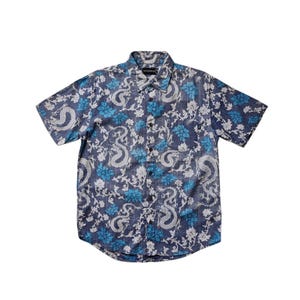 Puede incluir: Una camisa azul de manga corta con botones y un estampado floral blanco y azul con dragones.