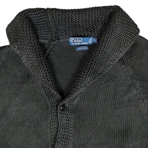 May include: A dark green knitted cardigan with a shawl collar and button closure. The label reads "Polo by Ralph Lauren" and "100% Cotton".