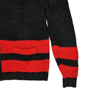 May include: Black and red striped sweater with a pocket on the front. The sweater is made of a knitted fabric.