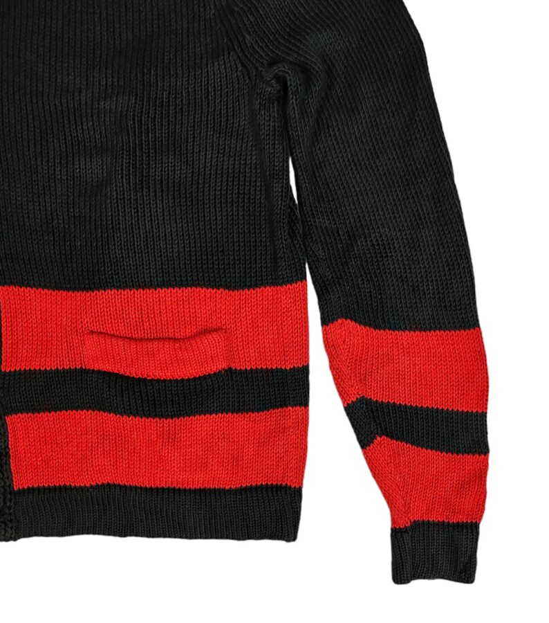 May include: Black and red striped sweater with a pocket on the front. The sweater is made of a knitted fabric.