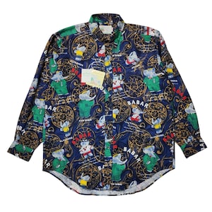 May include: A long-sleeved button-down shirt with a navy blue background and a repeating pattern of Babar the Elephant characters in various outfits. The design includes compass-like shapes and the word "BABAR".