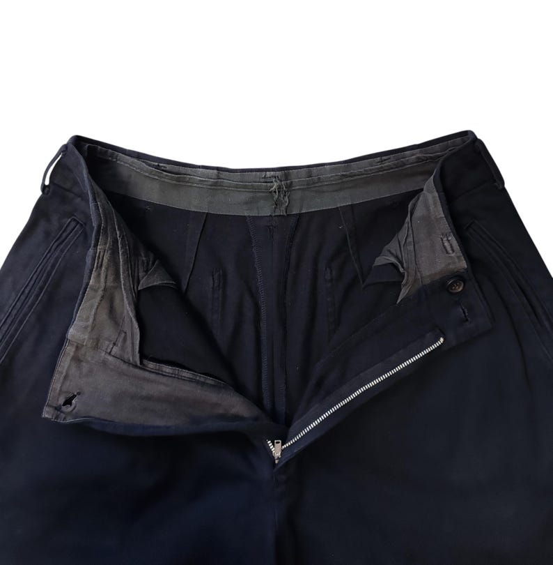 Puede incluir: Primer plano de pantalones azul marino con cremallera abierta y cierre de bot&oacute;n. Los pantalones tienen un dise&ntilde;o cl&aacute;sico con costuras visibles y una cinturilla reforzada. El forro interior es visible.