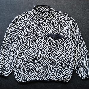 Pode incluir: Uma camisa de manga comprida com estampa de zebra em preto e branco, com gola alta e fecho de botão preto.