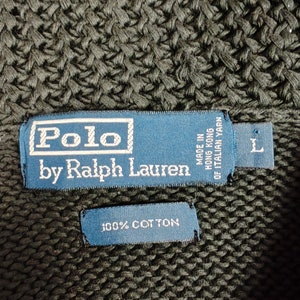 May include: A dark green knitted sweater with a blue label that reads "Polo by Ralph Lauren" and "Made in Hong Kong of Italian Yarn". The label also has a size "L" tag. A smaller blue label reads "100% Cotton".
