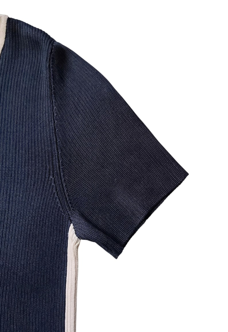 May include: A short-sleeved ribbed knit top in dark navy blue featuring a contrasting cream-colored vertical stripe along the side seam and a matching cream-colored trim along the neckline edge, constructed with a fine vertical texture.