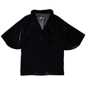 May include: A black velvet short-sleeved jacket with a collar and a single button closure. The jacket has a label with the text "WILFRED" on it.